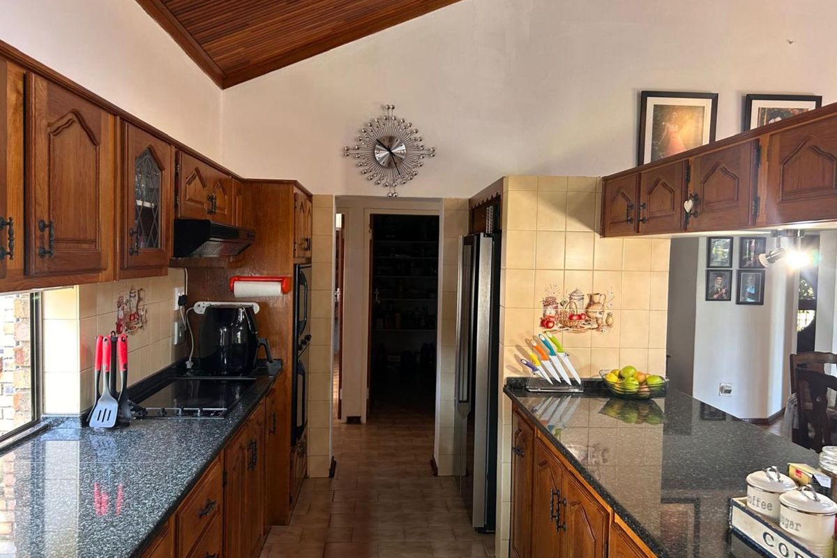 A traditional kitchen featuring dark wood cabinetry, granite countertops, tiled splashbacks, and a vaulted timber-paneled ceiling, leading into a separate scullery or pantry area.