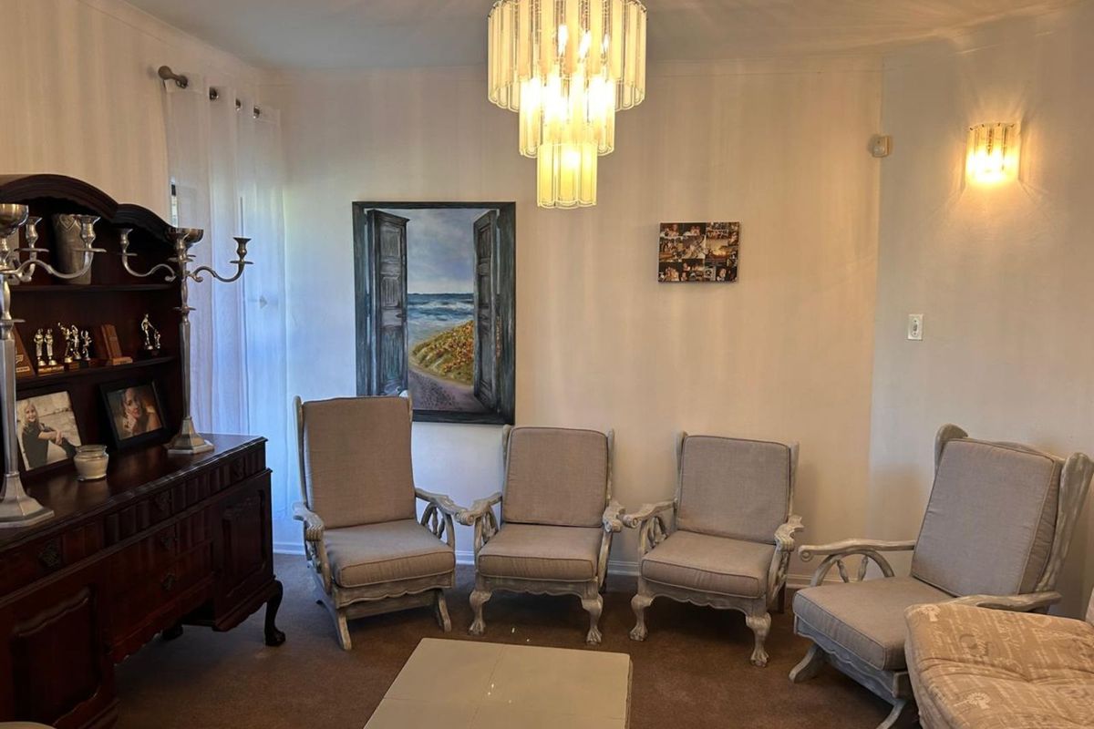 A living room featuring a tiered glass chandelier, wall-mounted lighting, and carpeted flooring.