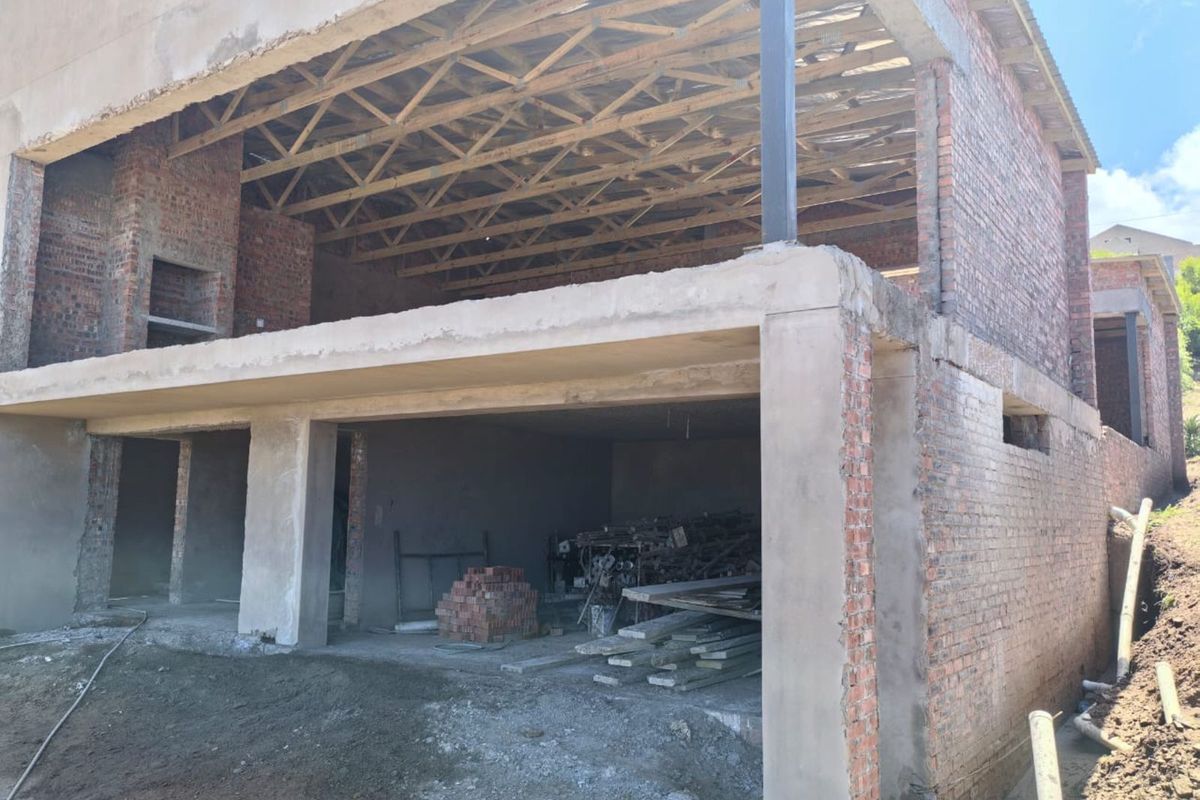 A two-story residential property currently under construction, featuring exposed brickwork, concrete structural elements, and open roof trusses.