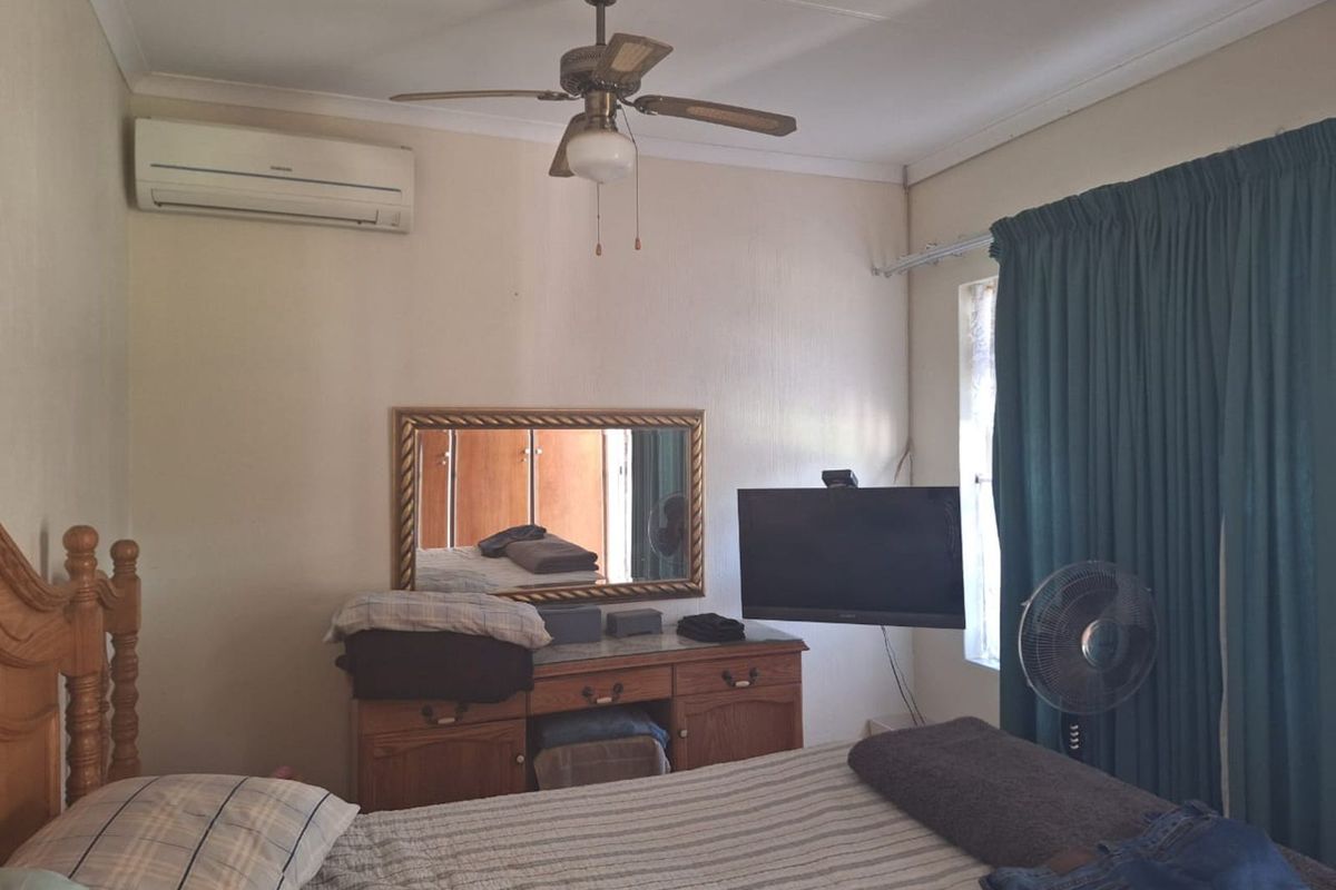 A functional bedroom featuring a ceiling fan, wall-mounted air conditioning unit, and built-in cabinetry.