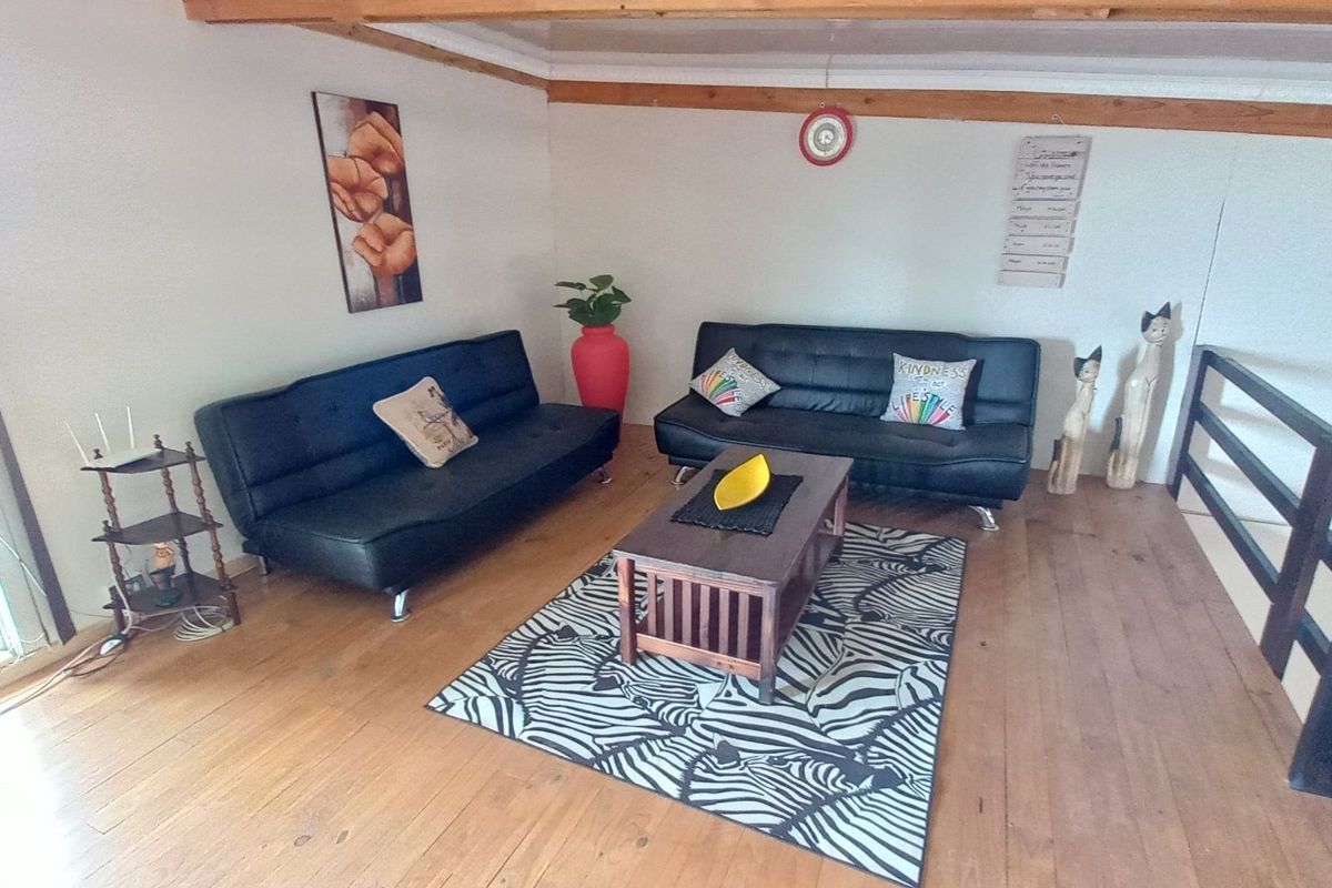 A spacious loft-style living area featuring exposed timber ceiling beams and polished wooden flooring, providing a warm and rustic atmosphere.