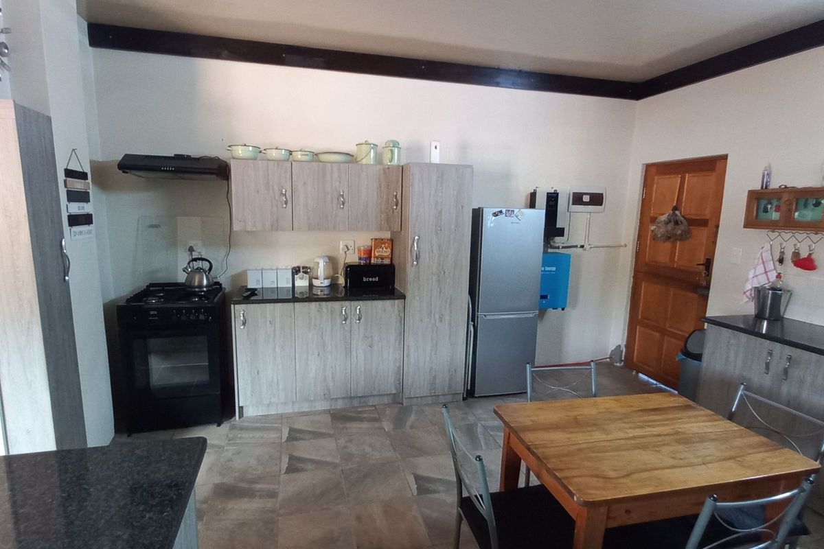 A functional kitchen featuring wood-look cabinetry, dark countertops, a built-in oven with extractor fan, and tiled flooring, with an adjacent dining area.