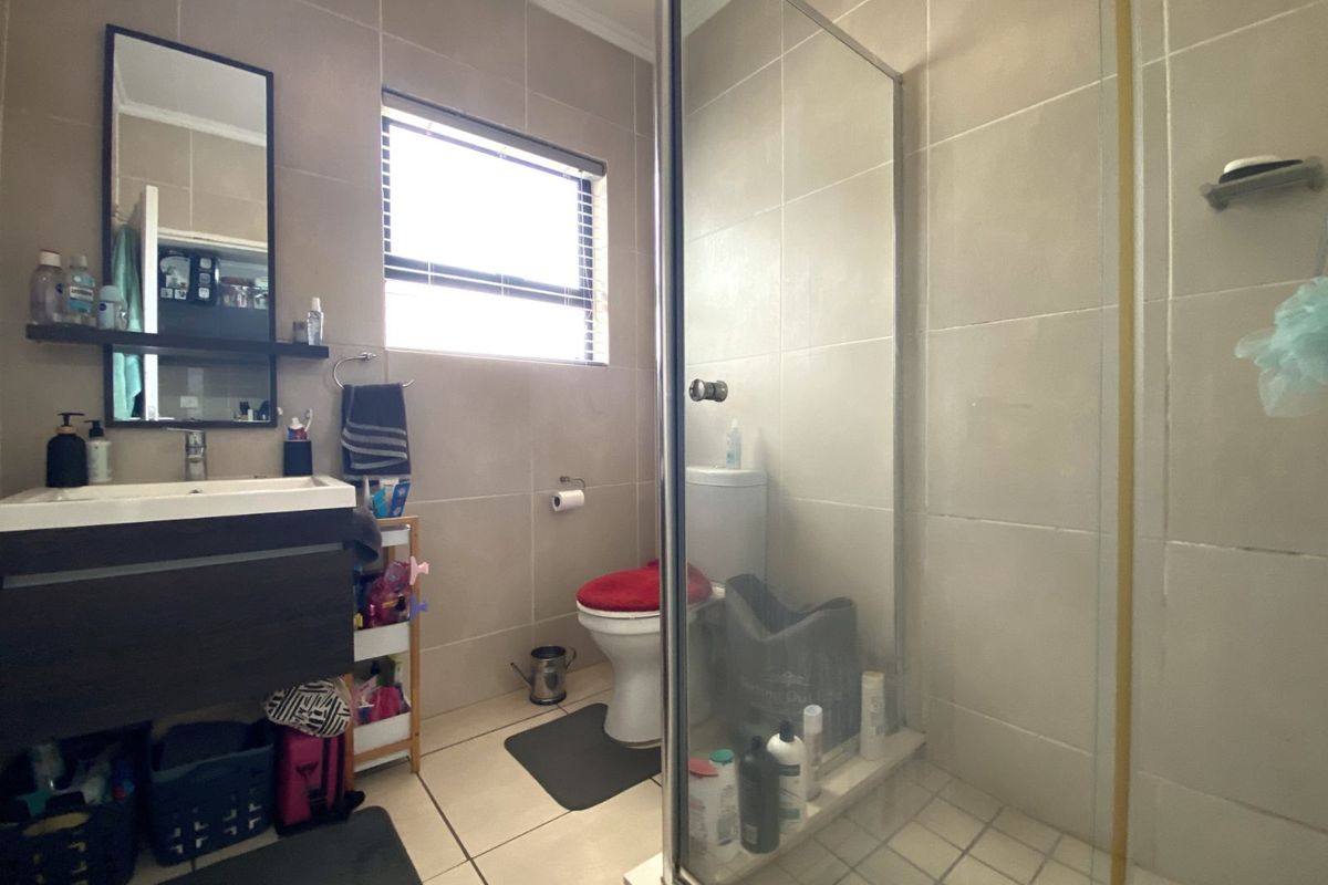 A functional bathroom featuring a glass-enclosed shower, wall-mounted vanity with basin, and tiled flooring throughout.