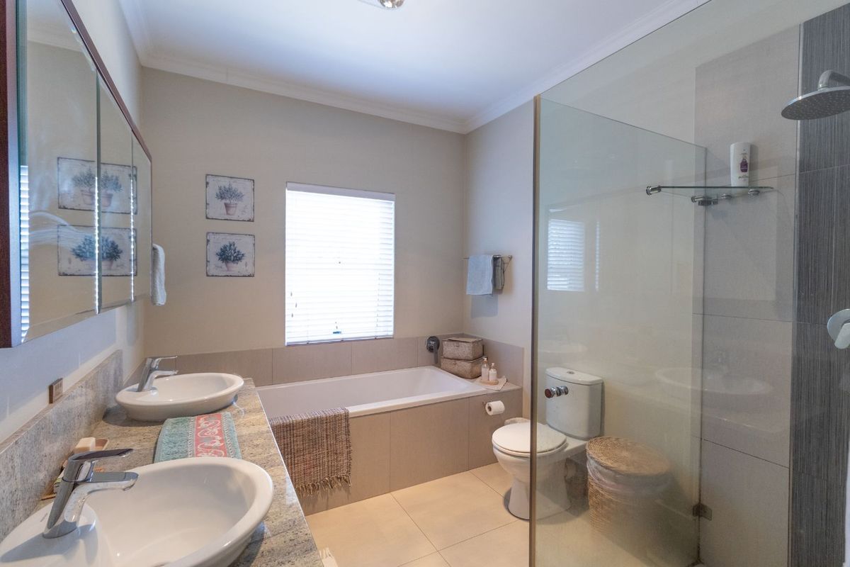 Modern bathroom featuring a double vanity with stone countertop, a built-in bathtub, and a separate glass-enclosed shower with a rainfall showerhead.