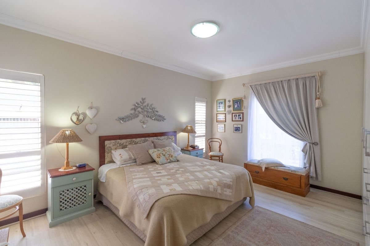 A well-maintained bedroom featuring light-toned wood-look flooring, plantation shutters, and neutral wall finishes, providing a comfortable and bright living space.