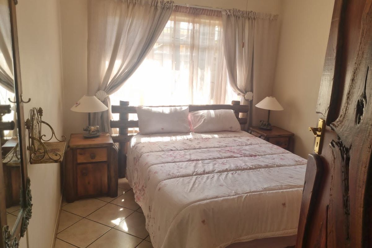 A cozy bedroom featuring tiled flooring, a ceiling fan, and a window with curtains, providing a functional and comfortable sleeping space.