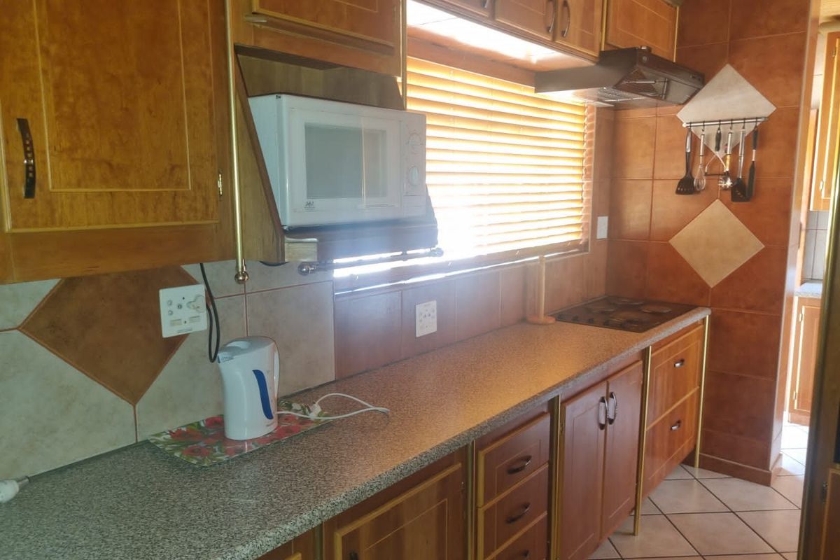 A functional kitchen featuring wooden cabinetry, tiled splashbacks, a built-in hob, and an integrated extractor fan with ample counter space.
