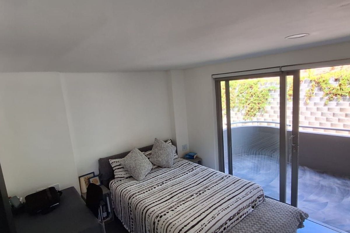 A bright bedroom featuring sliding glass doors that open onto a private balcony with a retaining wall view.