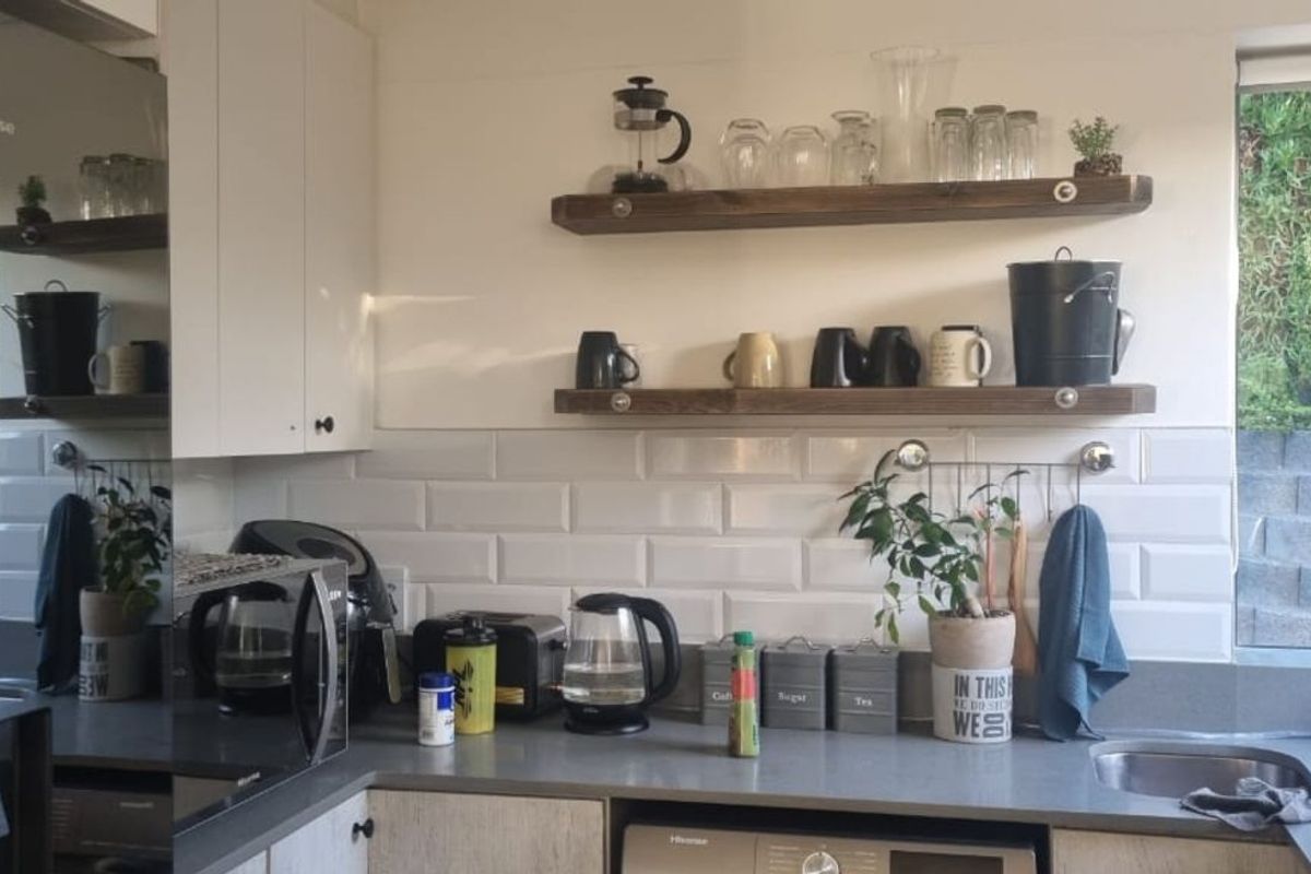 A functional kitchen featuring white cabinetry, subway tile backsplash, dark countertops, dual sinks, and open timber shelving.
