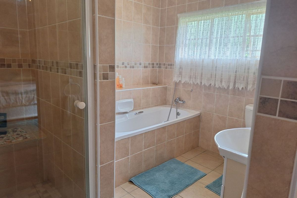 A functional bathroom featuring a built-in bathtub, a separate glass-enclosed shower, and neutral wall-to-floor tiling.