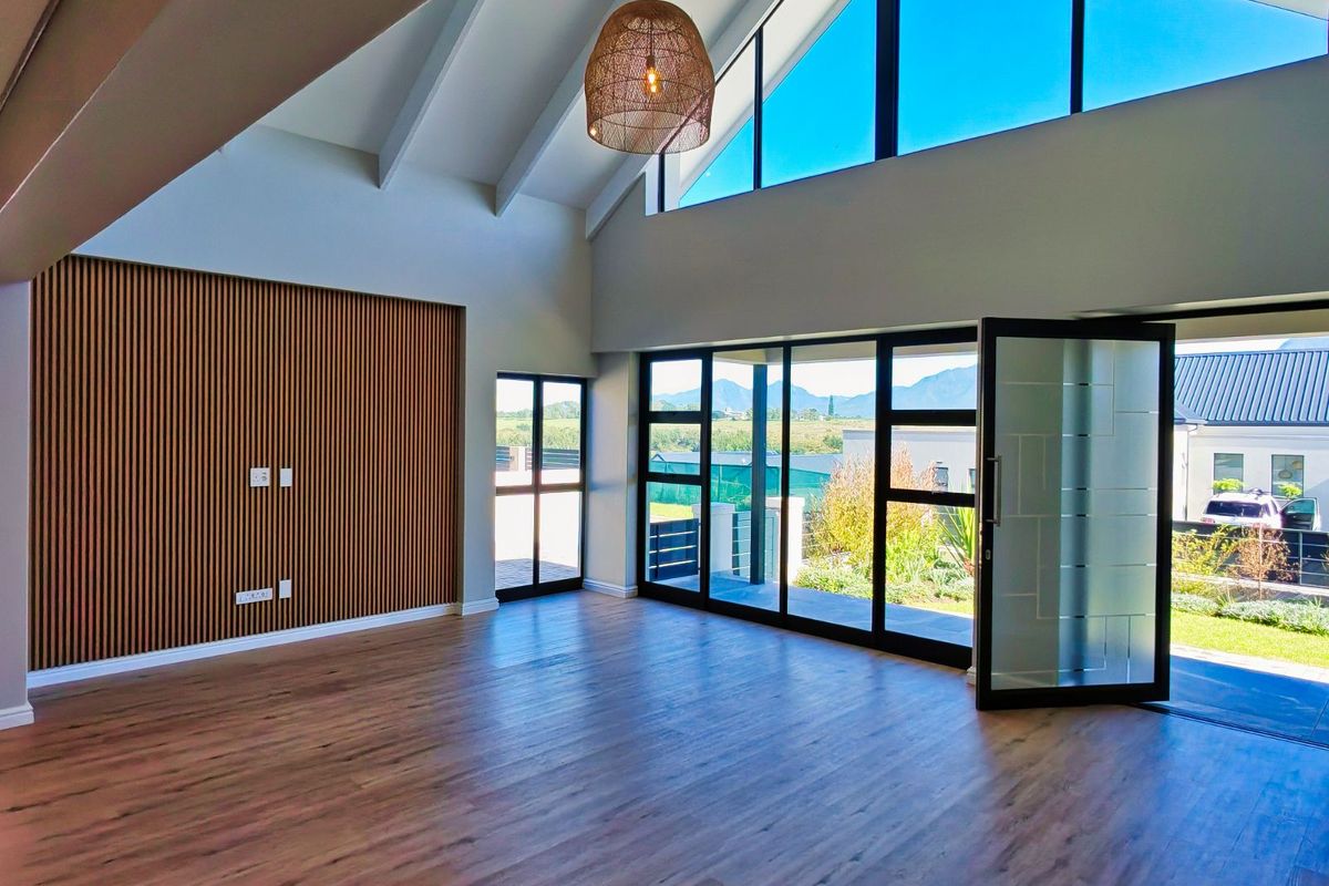 Spacious living area featuring high vaulted ceilings, timber slat feature wall, and large glass doors opening to a scenic outdoor patio.