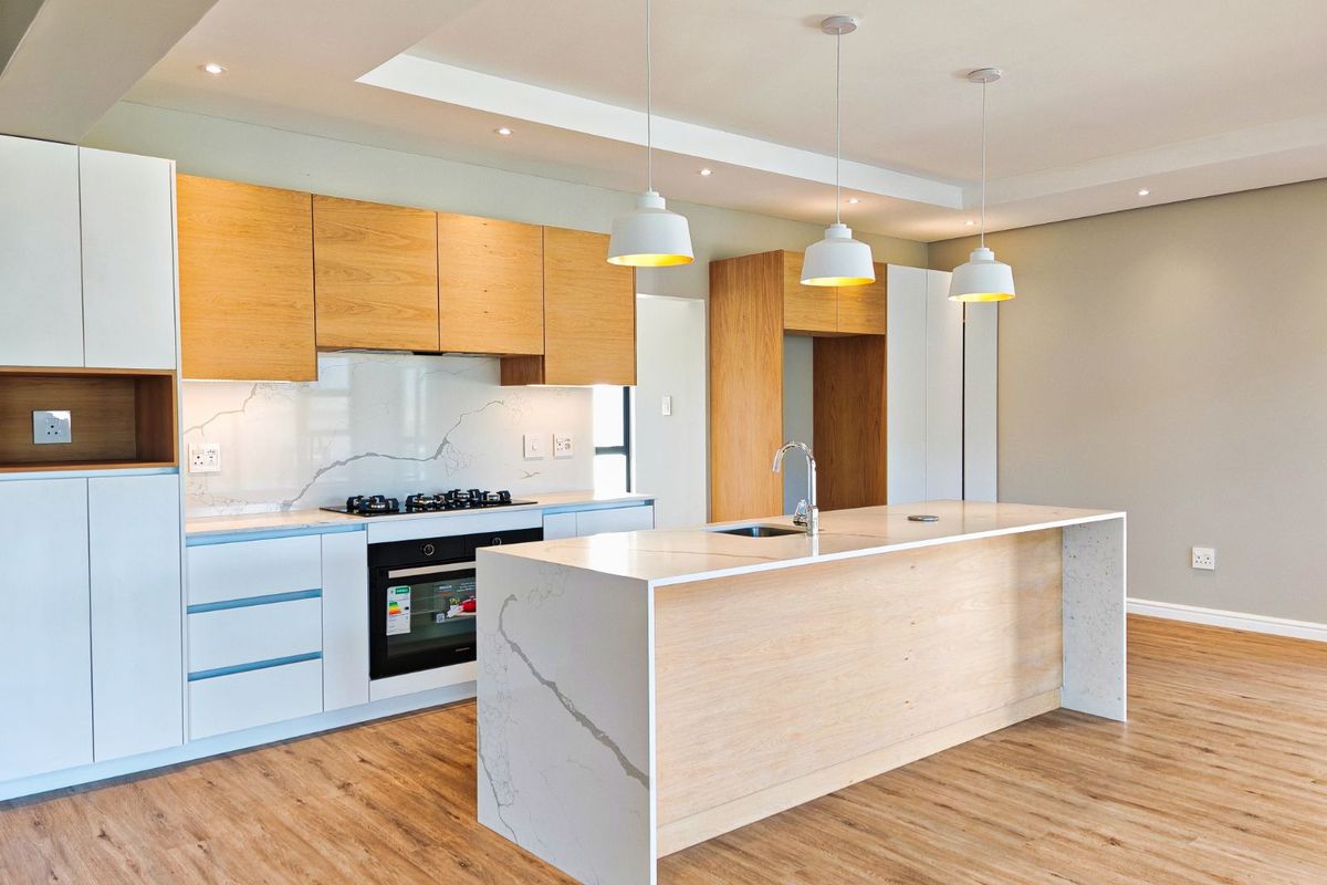 Modern open-plan kitchen featuring a large central island with stone countertops, integrated cabinetry, built-in oven, gas hob, and contemporary pendant lighting.
