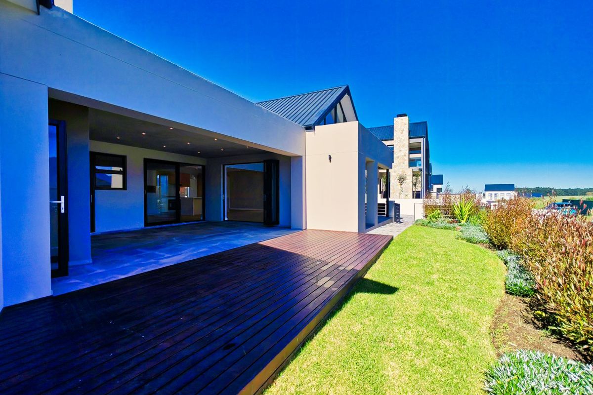 A modern rear exterior view featuring a spacious covered patio, timber decking, and a well-maintained garden with a clear blue sky.