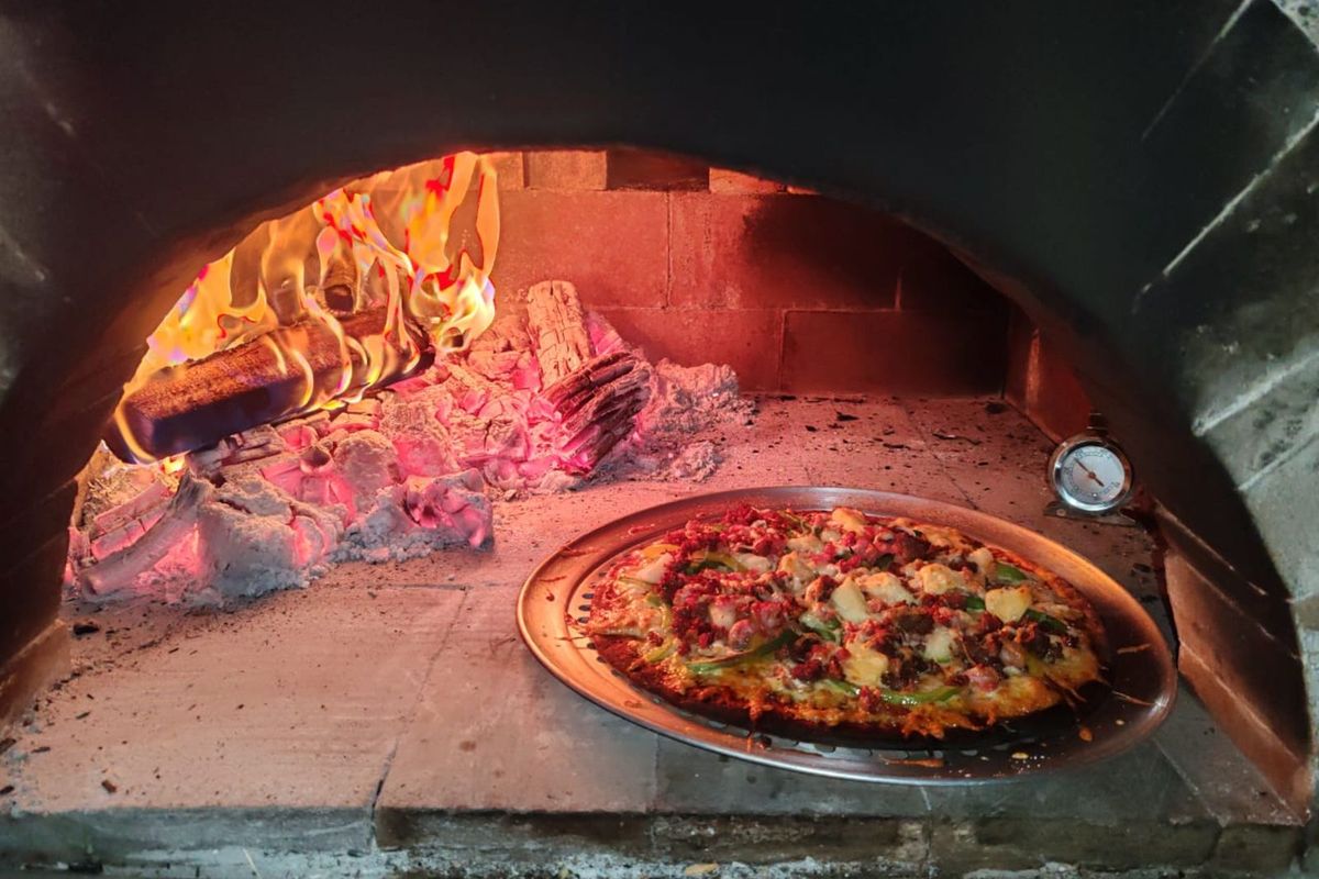 A built-in wood-fired pizza oven featuring a stone hearth, integrated thermometer, and active fire for authentic cooking.