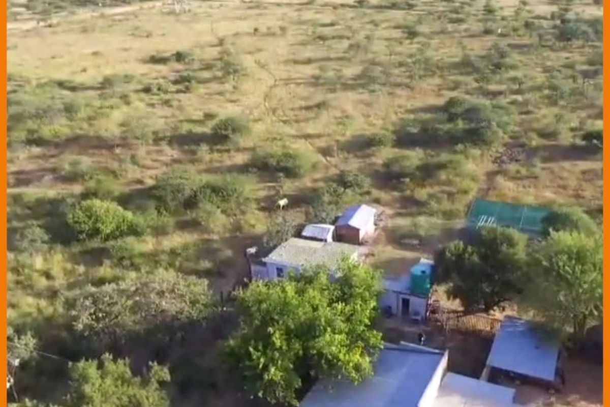 Aerial view of a rural property featuring multiple small structures, corrugated metal roofing, and a water storage tank set within a natural landscape.