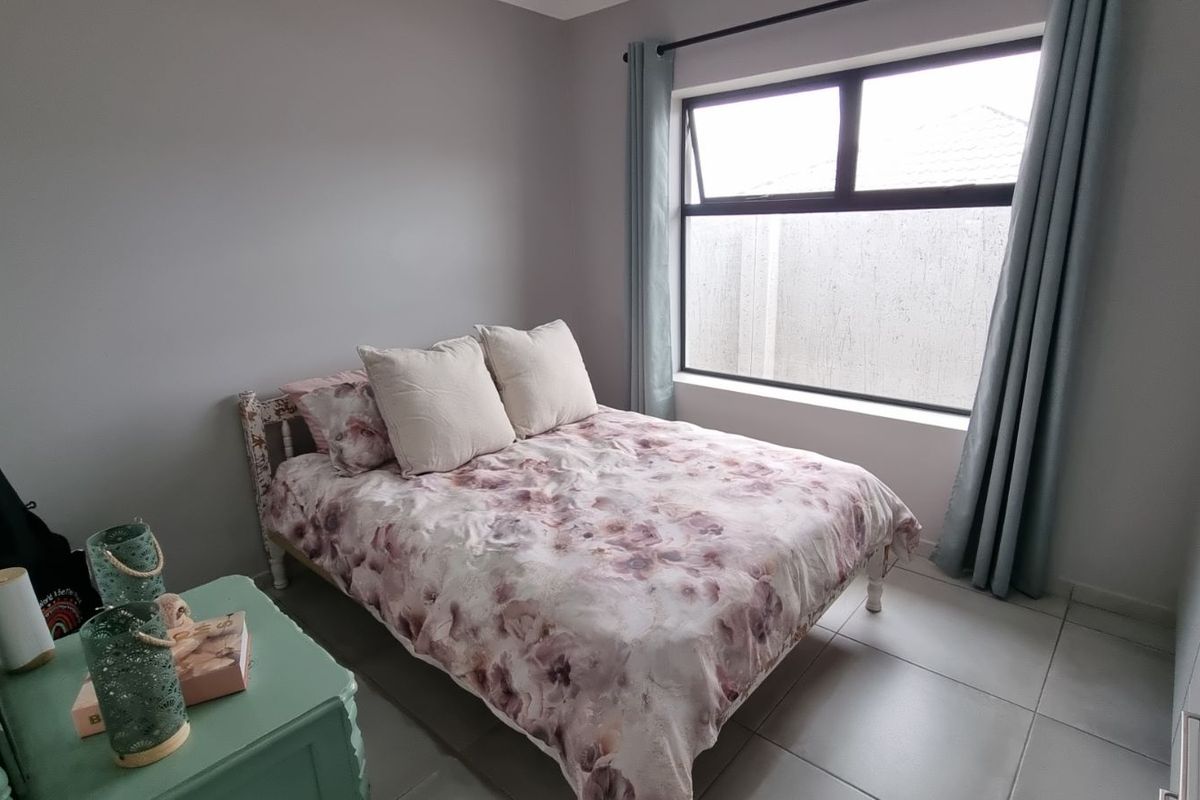 A well-maintained bedroom featuring neutral wall tones, large format floor tiles, and a window with integrated curtain tracks.