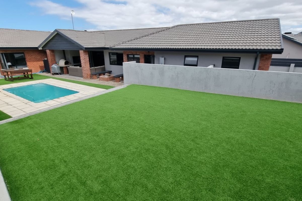 Rear garden featuring a swimming pool, paved patio area, and a large artificial lawn enclosed by a concrete boundary wall.