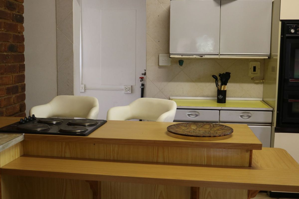 A dated kitchen featuring a wooden breakfast bar with an integrated electric hob, built-in oven, and traditional cabinetry.