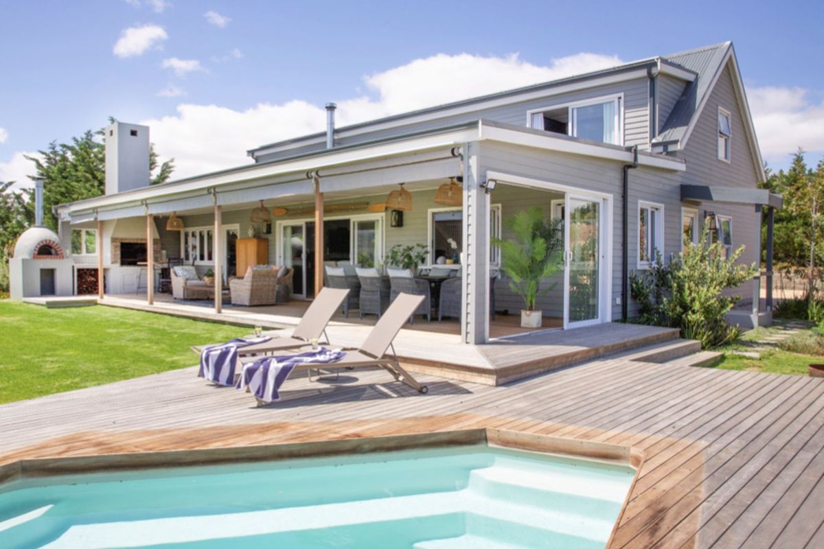 Spacious rear exterior featuring a large covered patio, built-in outdoor fireplace, pizza oven, and a wooden deck surrounding a swimming pool.