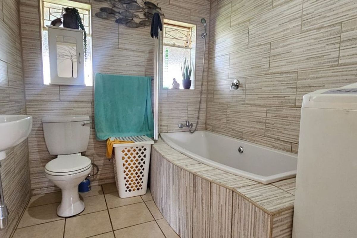 A functional bathroom featuring a built-in bathtub, pedestal basin, and toilet with floor-to-ceiling tiled walls.