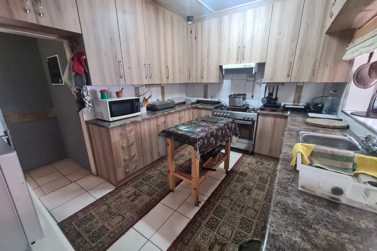 A functional kitchen featuring wood-look cabinetry, laminate countertops, a stainless steel sink, and a built-in gas stove with an extractor fan.