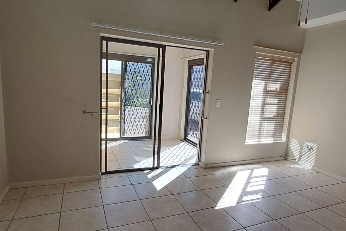 A bright living area featuring tiled flooring, vaulted ceilings, and sliding glass doors leading to an outdoor patio space.