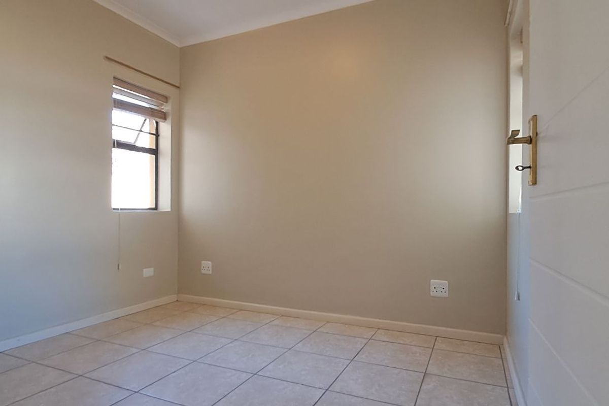 A clean, empty bedroom featuring neutral wall paint, tiled flooring, and a window with fitted blinds.