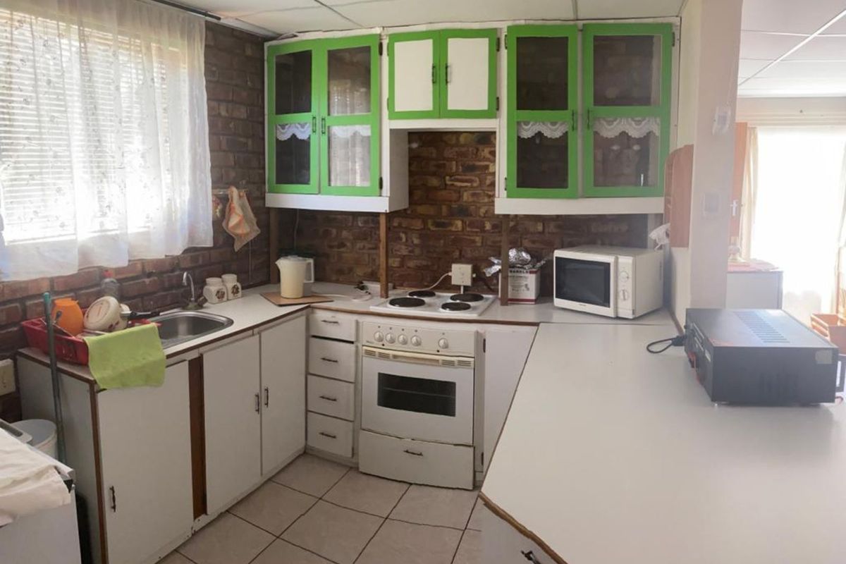 A dated kitchen featuring exposed brick walls, white cabinetry with green accents, tiled flooring, and a built-in oven and hob.