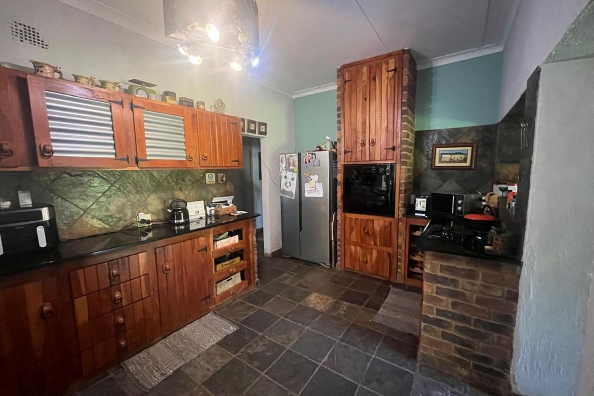 A rustic kitchen featuring timber cabinetry, dark stone countertops, slate tile flooring, and a built-in oven unit with brick detailing.