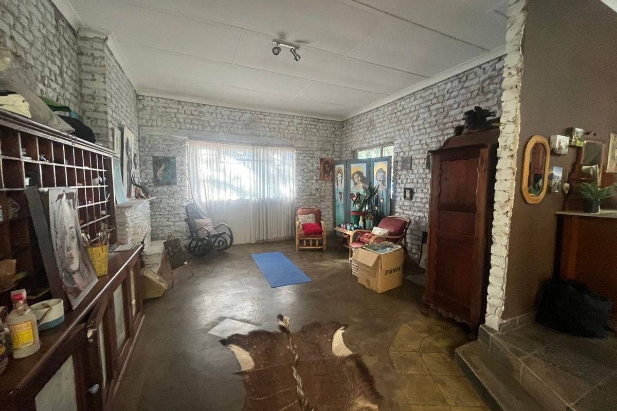 A spacious living room featuring exposed white-painted brick walls, concrete flooring, and a built-in fireplace, offering a rustic and character-filled living space.