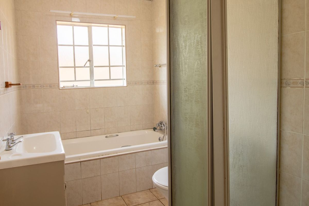 A functional bathroom featuring a built-in bathtub, a separate shower enclosure, and a vanity basin with tiled walls and flooring.