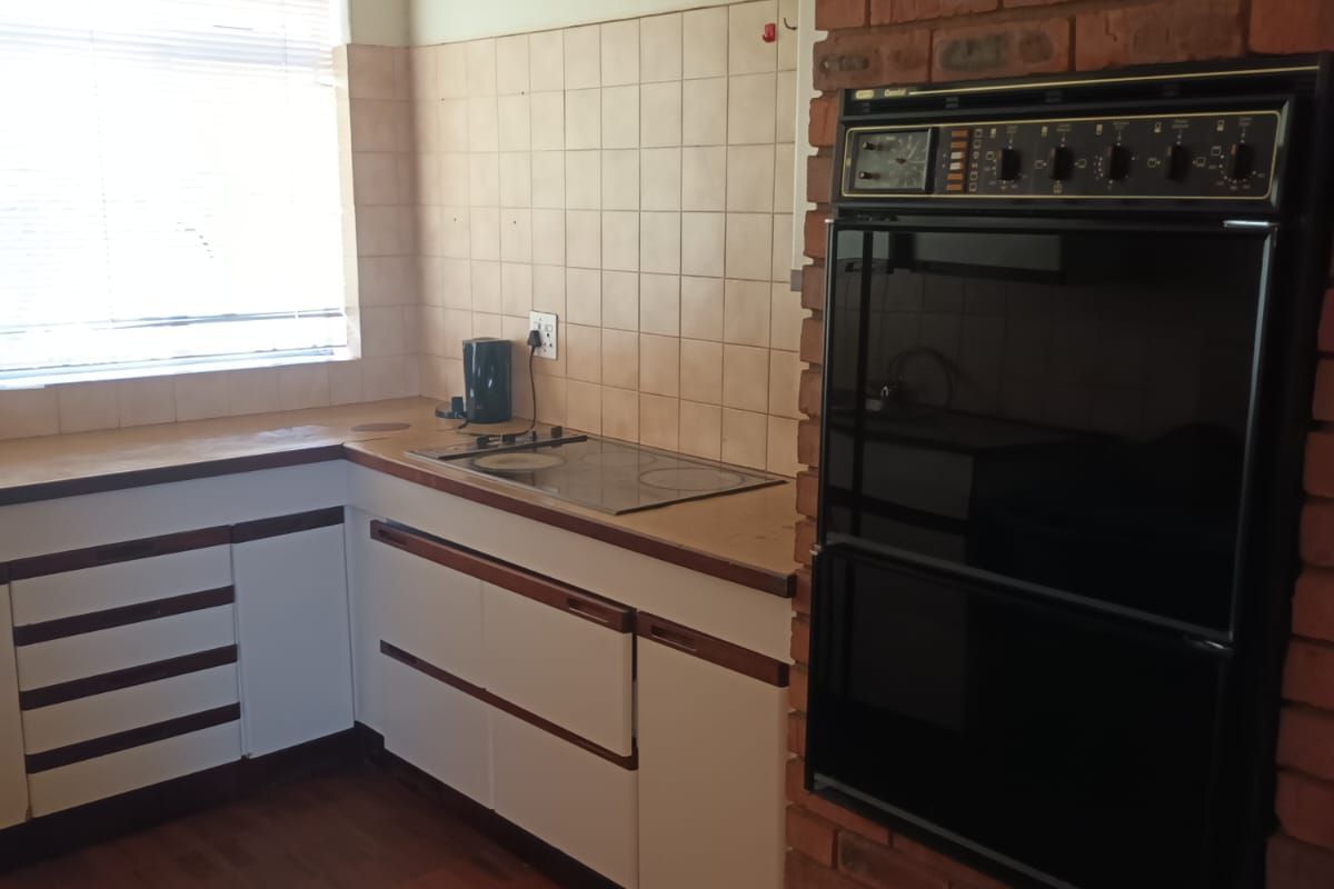 A functional kitchen featuring built-in cabinetry, a brick-encased wall oven, a cooktop, and tiled flooring with a window providing natural light.