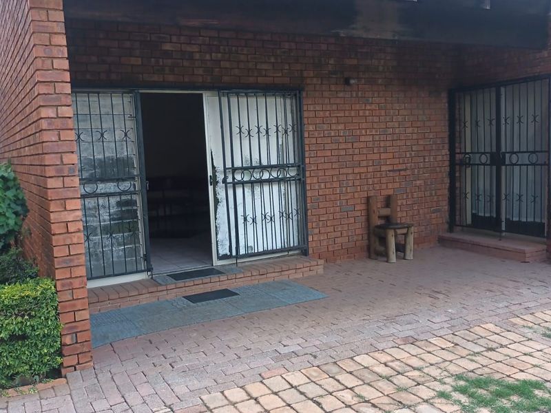 A covered brick patio area featuring paved flooring, security gates, and a brick chimney, providing a functional outdoor space for the home.