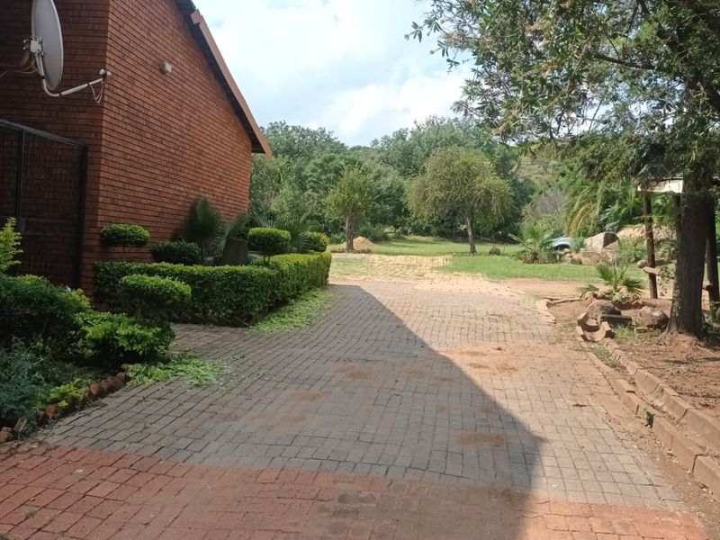 A view of the side exterior of the house featuring a brick facade, paved driveway, and landscaped garden area.