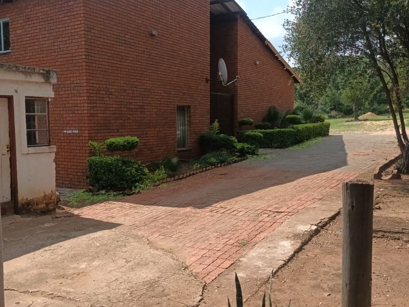 Exterior view of a red brick house featuring a paved driveway, landscaped hedges, and an adjacent outbuilding structure.