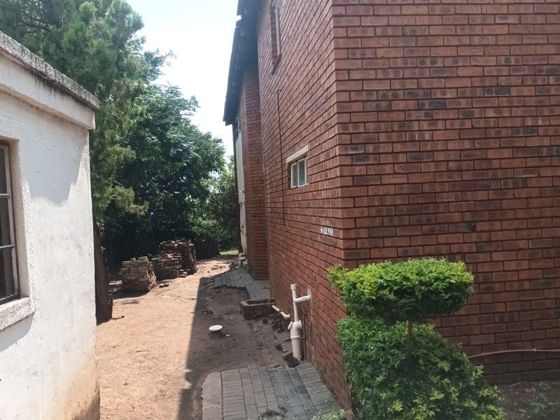 Side exterior view of the house showing exposed brickwork, paved walkway, and utility plumbing against the building structure.
