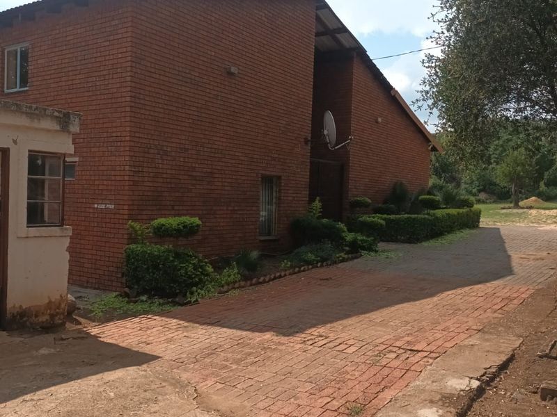 Exterior view of a brick house featuring a paved driveway, landscaped hedges, and a satellite dish mounted on the side wall.