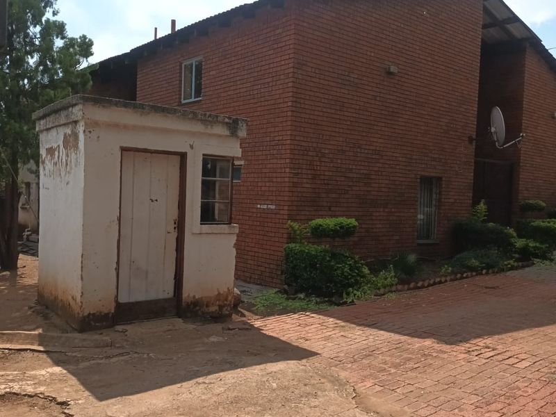 Exterior view of a brick house featuring a small detached utility structure, paved driveway, and mature landscaping.