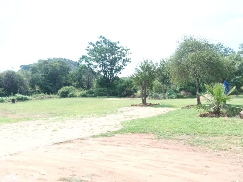 A view of the expansive rear garden featuring a paved patio area, established trees, and a large lawn.
