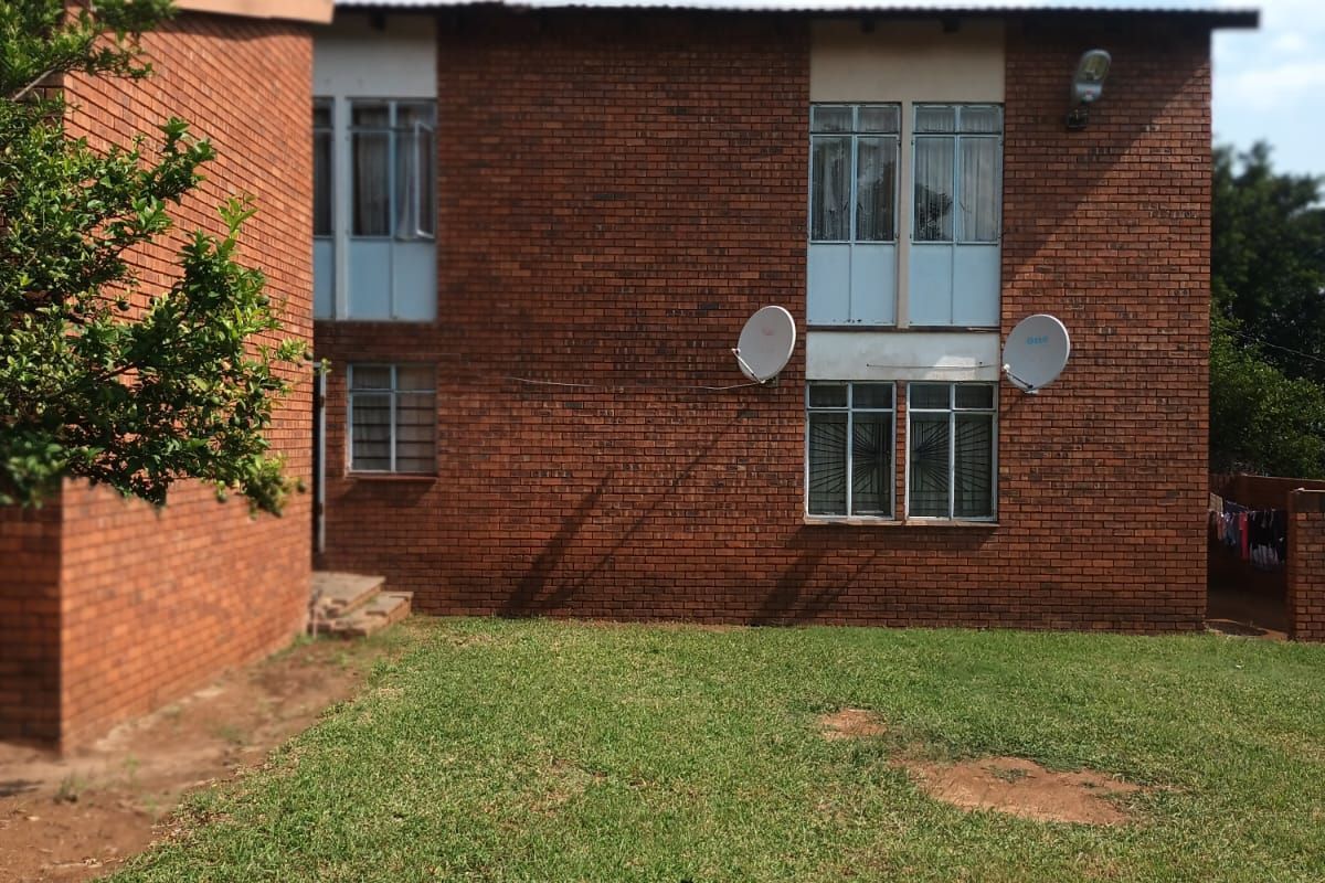 A view of the rear brick facade of the house, featuring multiple windows and a private garden area.
