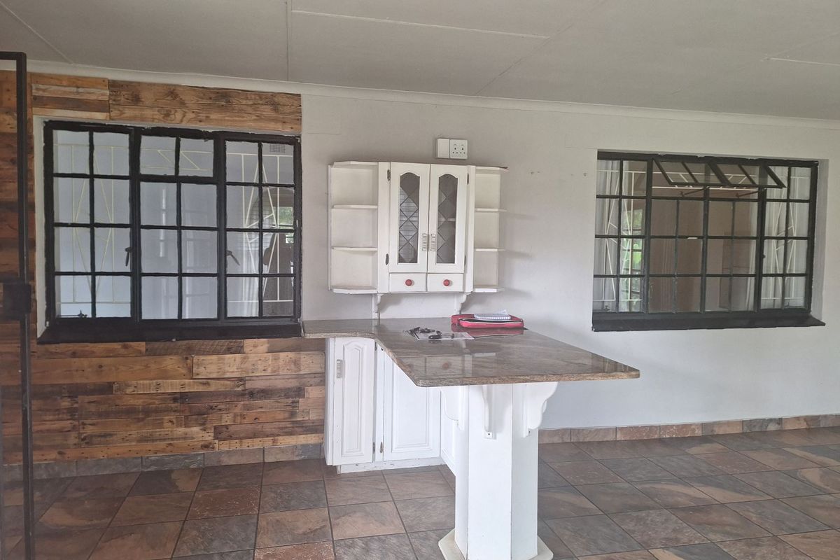 A kitchen area featuring a built-in breakfast bar, white cabinetry, and rustic wood-paneled wall accents with large metal-framed windows.