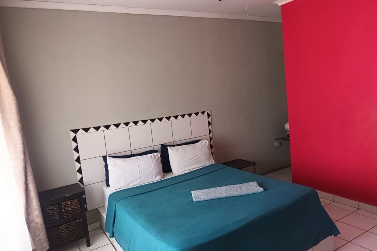 A bedroom featuring a tiled headboard wall, ceiling fan, and tiled flooring with a bold red accent wall.