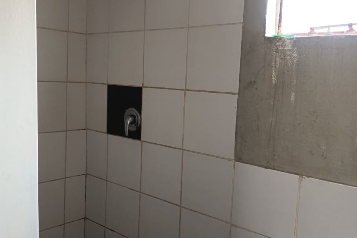 A functional bathroom space featuring a shower and basin, currently requiring cosmetic finishing and repairs to wall surfaces and fixtures.