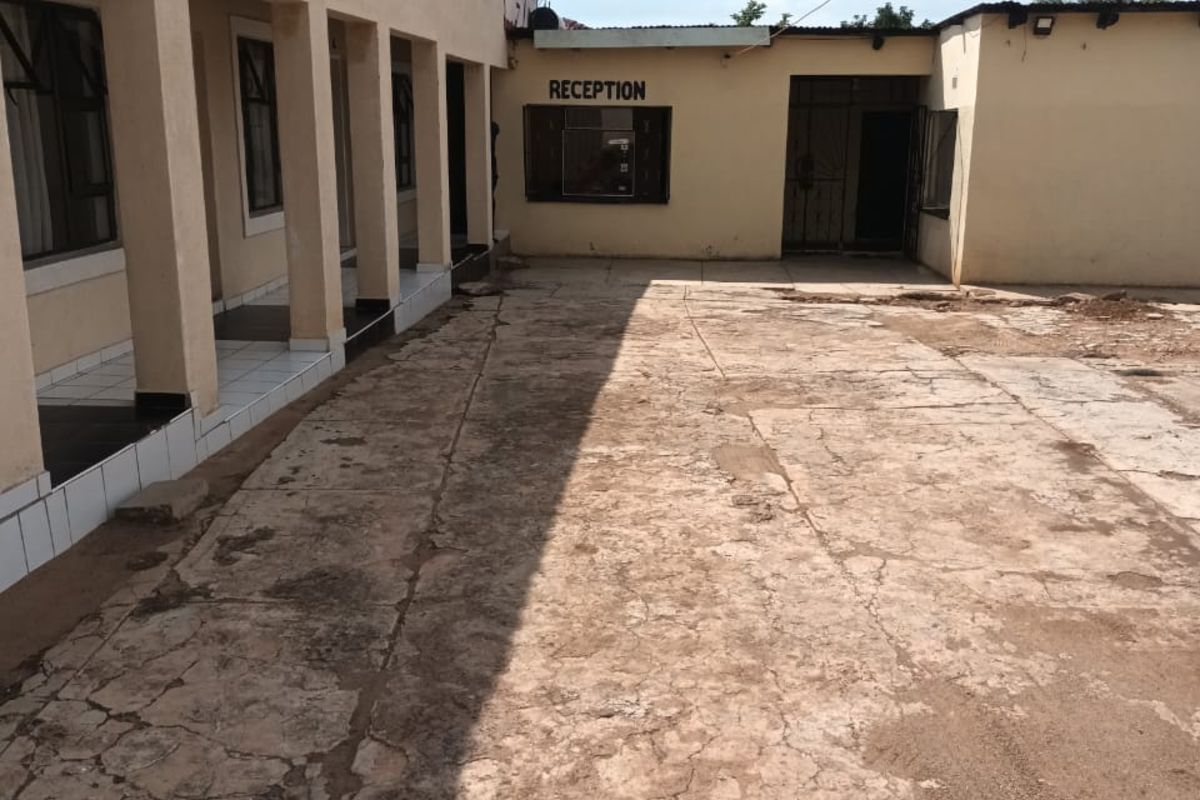 Exterior view of a business property featuring a reception entrance, covered walkway, and a large, weathered concrete courtyard area.