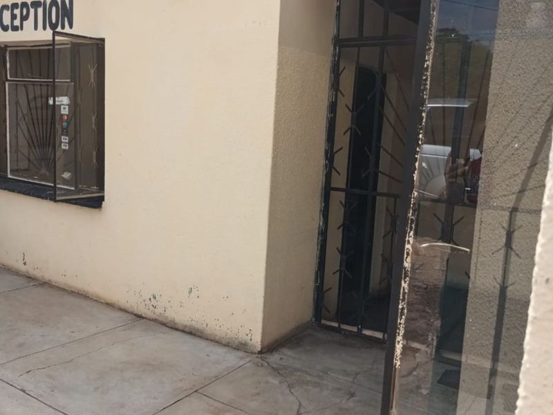 Exterior view of a business reception entrance featuring a security gate, window with security bars, and paved walkway.