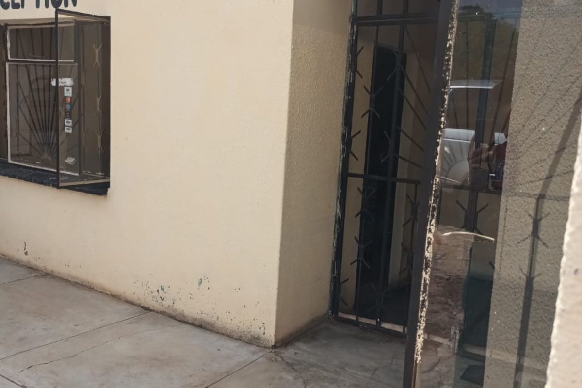 Exterior view of a business reception entrance featuring a security gate, window with security bars, and paved walkway.