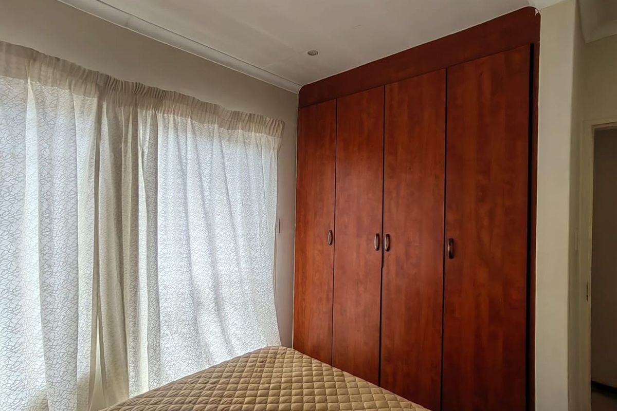 A bedroom featuring built-in wooden cupboards with a classic finish, providing ample storage space and natural light from the adjacent window.