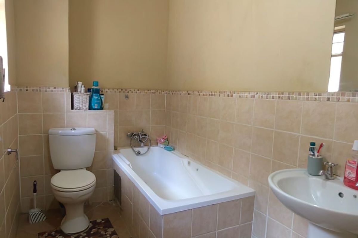 A functional bathroom featuring a built-in bathtub, pedestal sink, and toilet with neutral wall tiling and ceramic floor tiles.