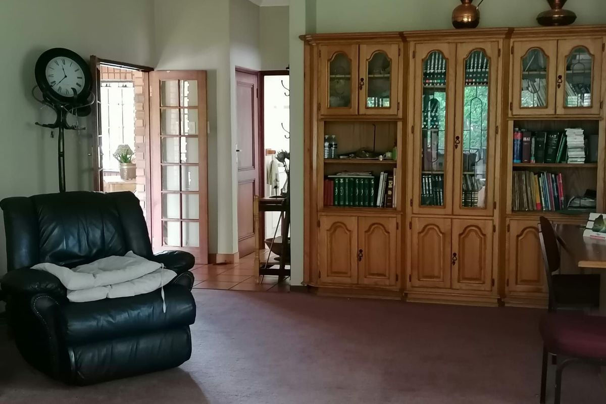 A living room featuring built-in wooden cabinetry, carpeted flooring, and access to an adjacent hallway and exterior area through glass-paneled doors.
