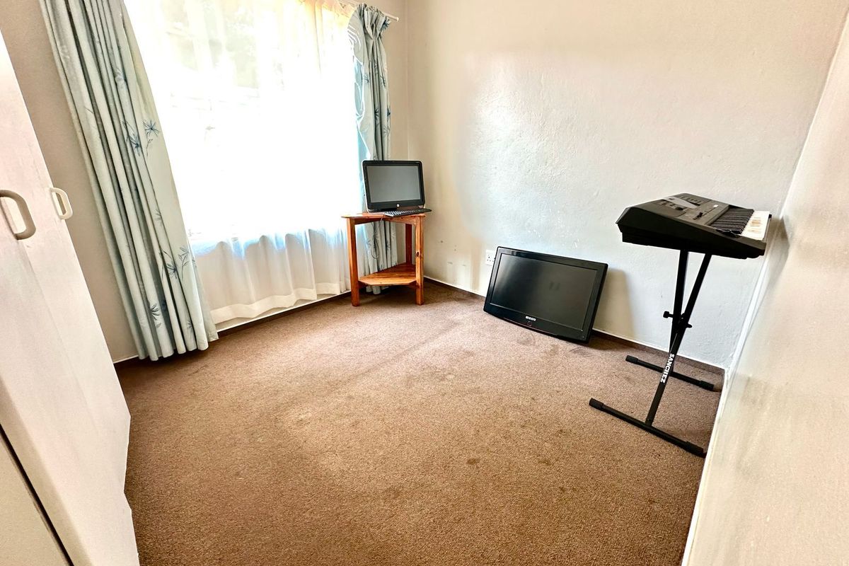 A bedroom featuring neutral walls, carpeted flooring, and a large window allowing natural light, providing a functional space for rest or study.